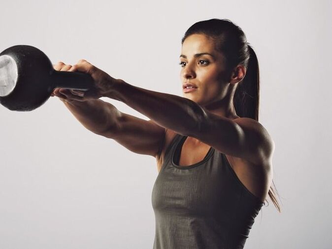 Dziewczyna wykonuje ćwiczenie powiększające piersi za pomocą odważnika Kettlebell